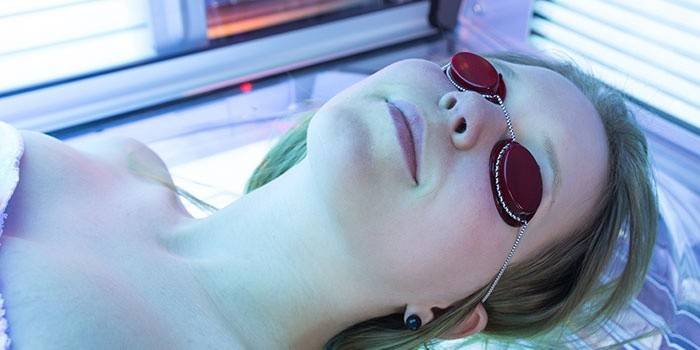 Menina sunbathes em uma cama de bronzeamento em copos