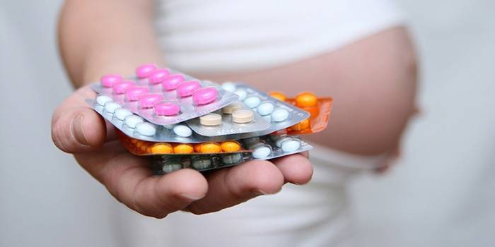 Tehotné dievča drží v ruke hormonálne tabletky
