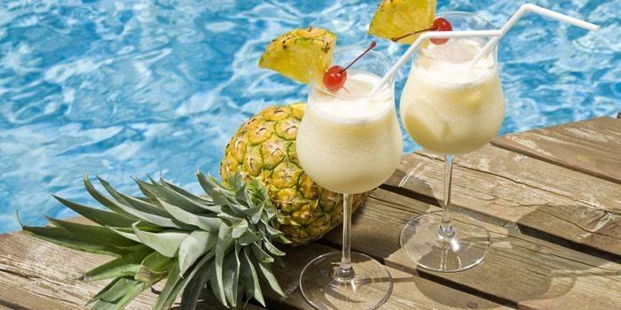 Dois copos com um cocktail e abacaxi