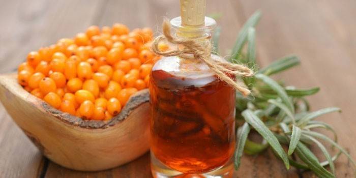 Óleo de espinheiro mar em uma garrafa e frutos de espinheiro mar num prato