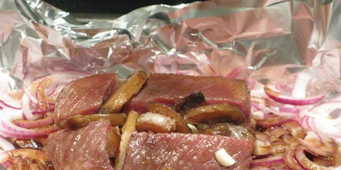 Trozos de carne con cebolla y papas en papel de aluminio antes de hornear
