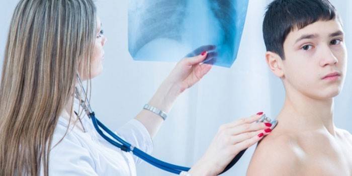 Medic escucha los pulmones de un adolescente y examina una radiografía.