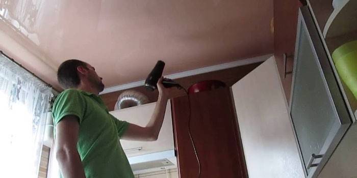 Secando o teto do estiramento após a inundação com um secador de cabelo