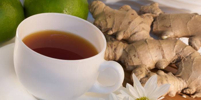 Té de jengibre en una taza, limas y raíz de jengibre