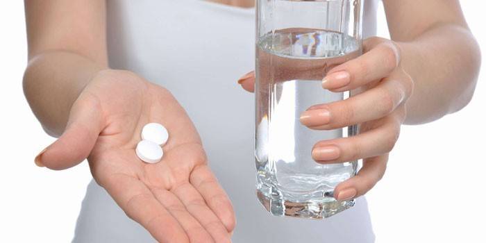 Niña sostiene pastillas en la palma y un vaso de agua