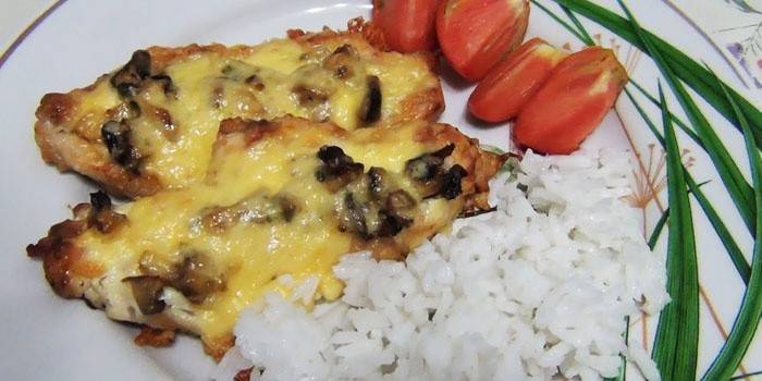 Chuletas preparadas con champiñones y queso y arroz hervido en un plato