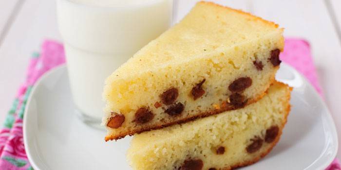 Um pedaço de bolo de semolina com passas em um prato e um copo de leite