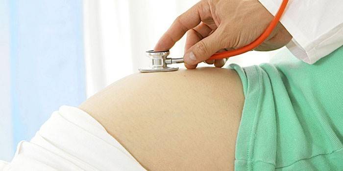 O médico ouve o batimento cardíaco fetal no abdômen de uma mulher grávida
