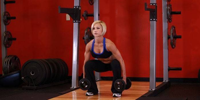 Chica realiza sentadillas con mancuernas en el gimnasio.