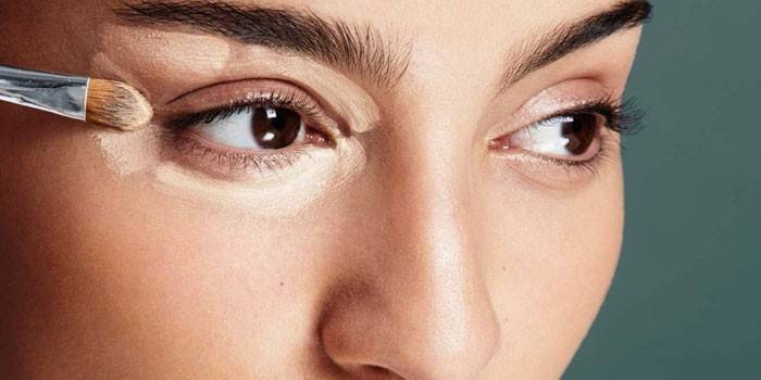Chica pone corrector alrededor de sus ojos