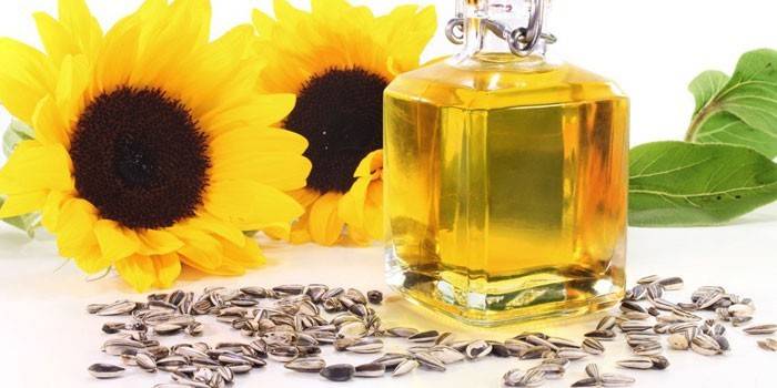 Aceite de girasol en un frasco de vidrio, flores y semillas de girasol.
