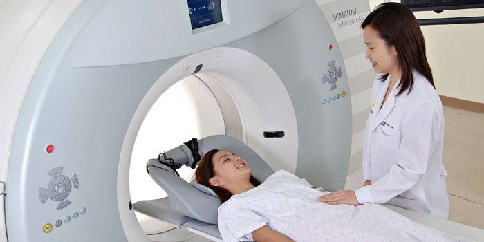 A menina no tomógrafo fala com o médico antes do estudo.