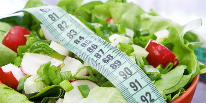 Ensalada de verduras en un plato y una cinta de centímetros