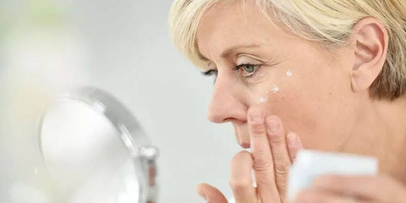 Mulher olhando no espelho e aplicar o creme no rosto
