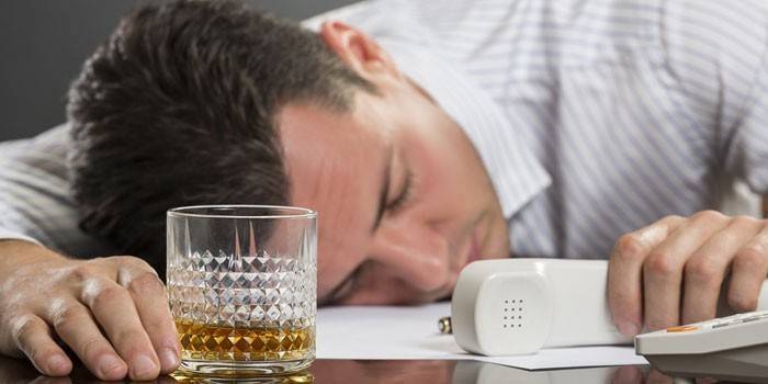Un hombre duerme en una mesa con un vaso y un teléfono.