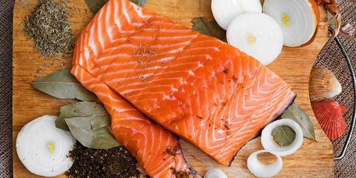Filé de salmão, cebola e especiarias em uma tábua de corte antes de salgar