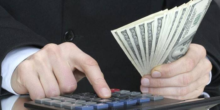 Mężczyzna liczy na kalkulator i trzyma w ręku banknoty