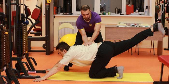 Un hombre con un entrenador realiza un ejercicio en el gimnasio.