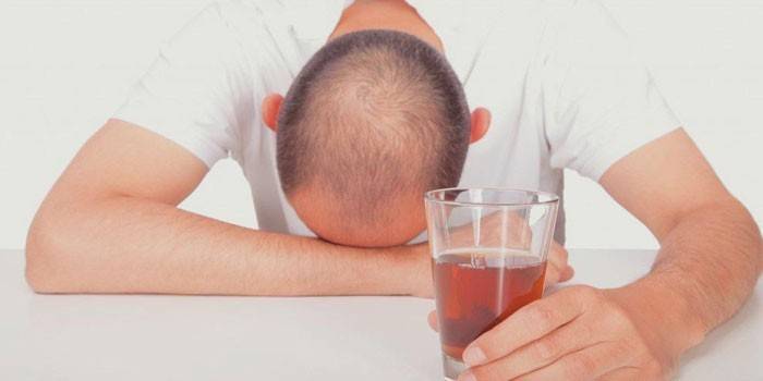 Um homem dorme em uma mesa com um copo de álcool