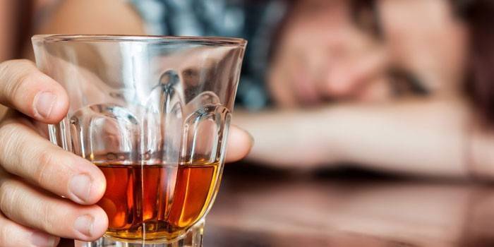 Un hombre duerme en una mesa y sostiene un vaso de whisky en la mano.