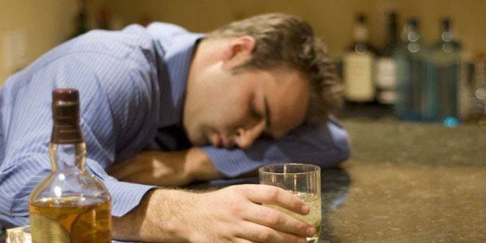 Muž spí na stole s pohárom alkoholu v ruke