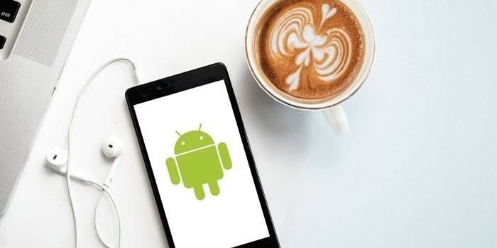 Smartphone so slúchadlami a šálkou kávy.