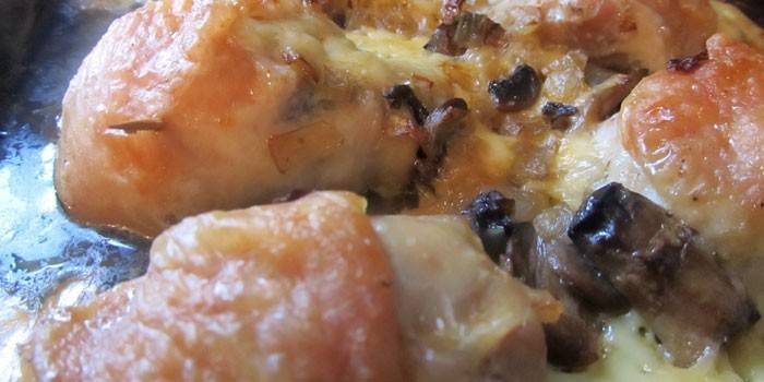Muslos de pollo listos con champiñones y queso en una bandeja para hornear