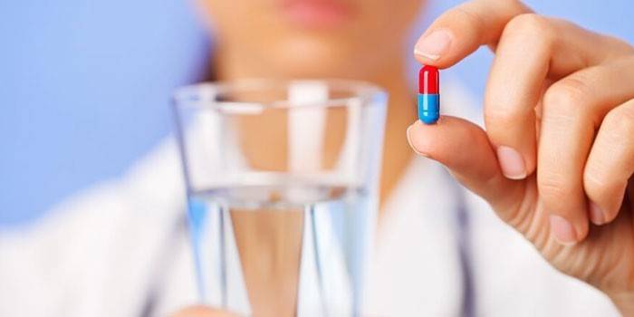 Uma cápsula e um copo de água nas mãos de um médico