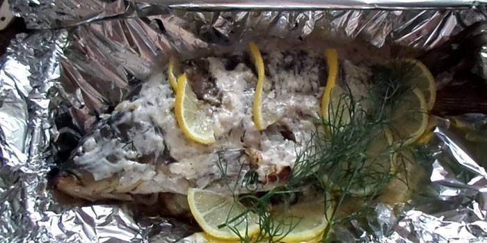 Carpa cruciana en papel de aluminio con crema agria y limón antes de hornear