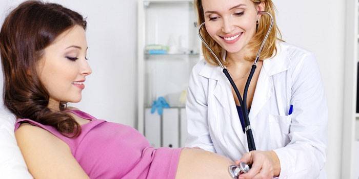 O médico ouve os batimentos cardíacos do bebê no estômago da mãe.