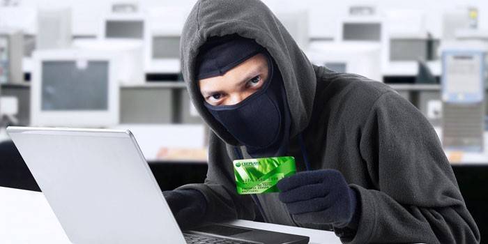 Cara mascarada atrás de um laptop e com um cartão na mão