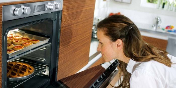 Menina olha para bolos no forno