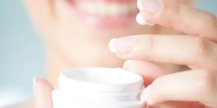 Creme em uma jarra e no dedo de uma mulher