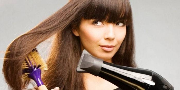 Niña seca el cabello con un secador de pelo