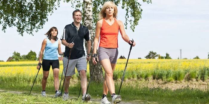Kobiety i mężczyźni uprawiają nordic walking.