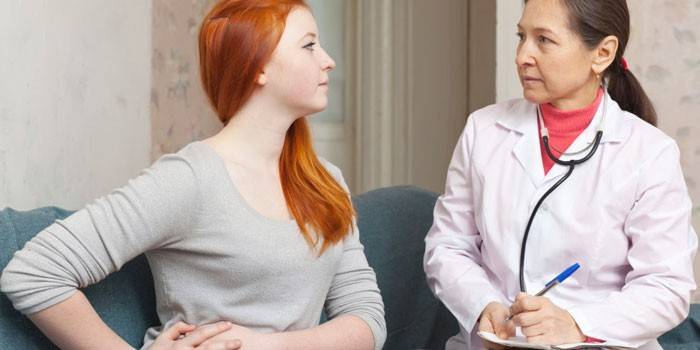Niña sostiene las manos sobre su lado derecho y habla con un médico