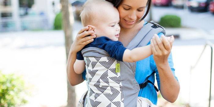 Niña con un niño en una mochila ergo