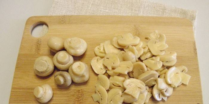 Champignon em conserva fatiado e inteiro em uma placa de corte