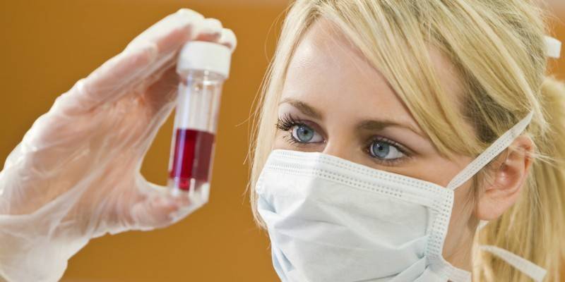 Tubo de ensayo con sangre en la mano de un asistente de laboratorio.