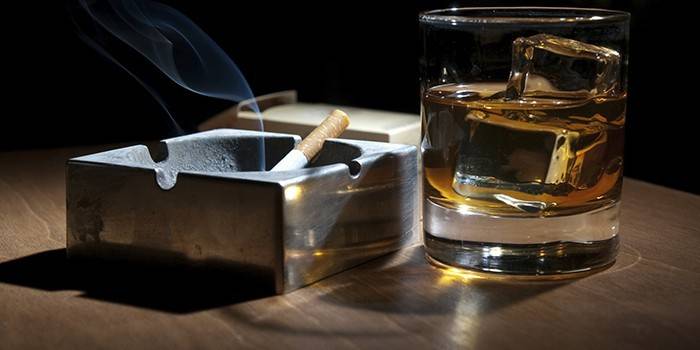 Um cigarro latente em um cinzeiro e um copo de álcool