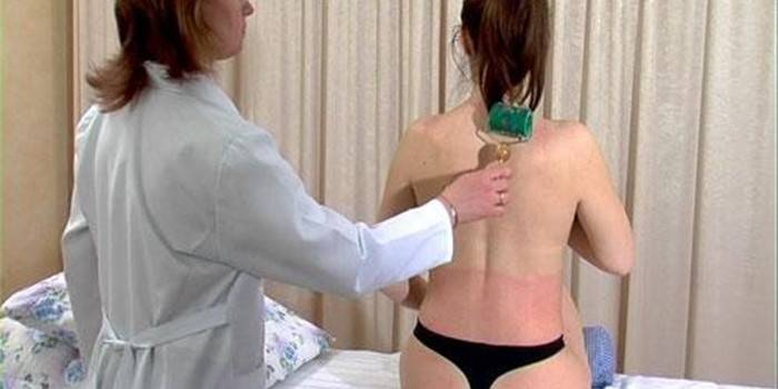 El médico le hace un masaje en el cuello a la niña con un aplicador de rodillos Kuznetsova