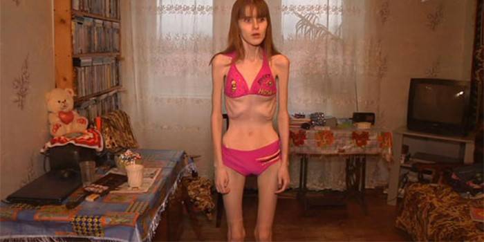 Uma menina com uma bulimia está de pé em uma sala em um maiô