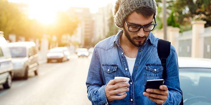 Cara com café e smartphone nas mãos