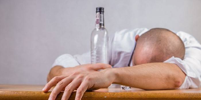 Muž leží na stole a prázdna fľaša alkoholu