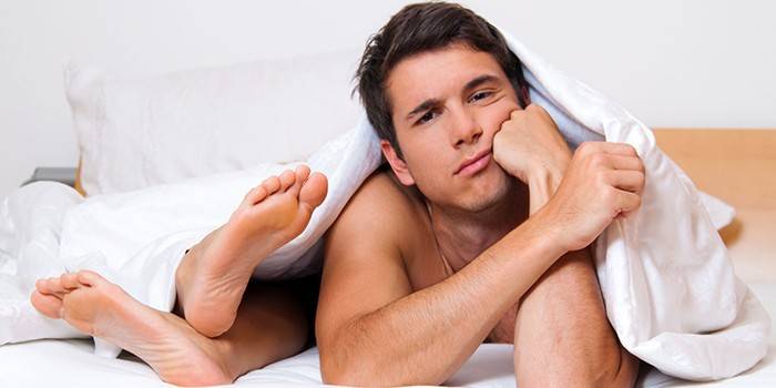 Homem na cama debaixo das cobertas e pés femininos