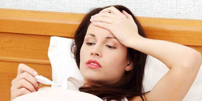 Uma mulher encontra-se na cama e olha para um termômetro