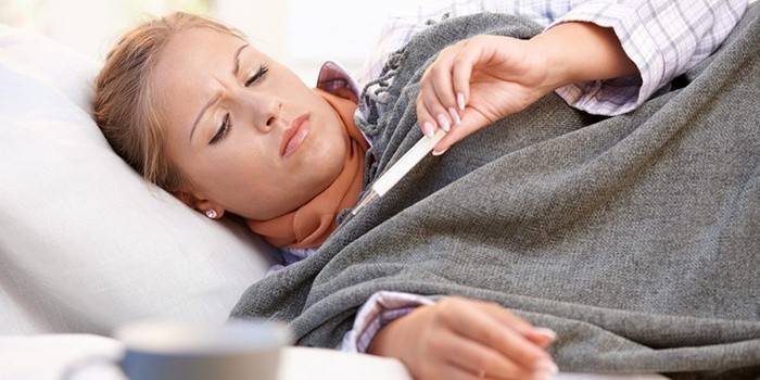 Uma mulher encontra-se na cama e olha para um termômetro