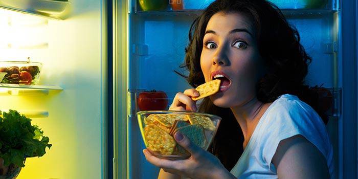 Niña comiendo galletas delante de un refrigerador abierto