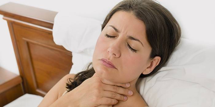 La mujer se acuesta en la cama y se lleva las manos a la garganta.