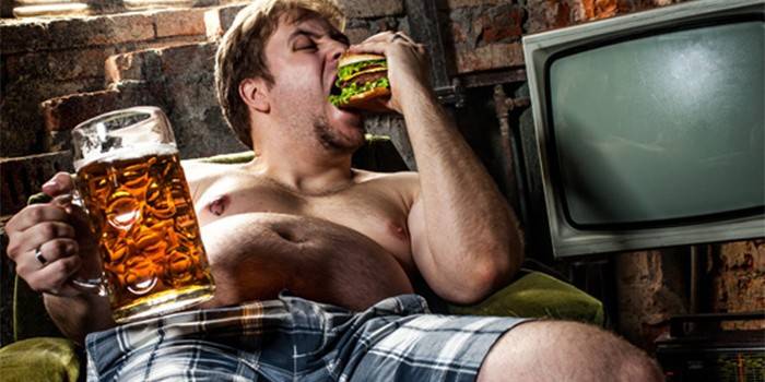 Homem comendo um hambúrguer e segurando um copo de cerveja